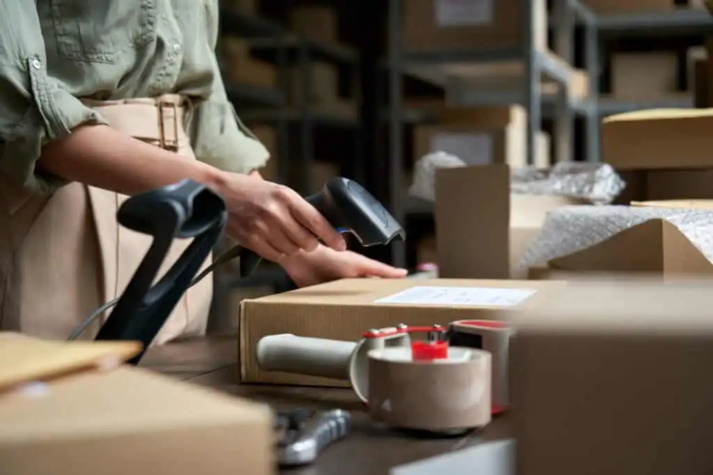 Female seller scanning ecommerce shipping box in dropshipping warehouse.
