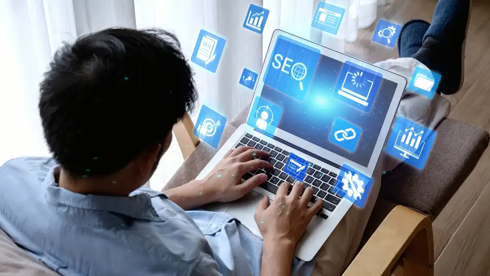 Person on a sofa typing on a laptop with floating blue icons representing SEO and analytics around the screen.